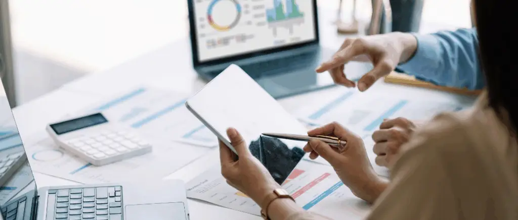 un homme et une femme assis autour d'un bureau font des calculs avec des outils numériques