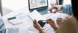 un homme et une femme assis autour d'un bureau font des calculs avec des outils numériques