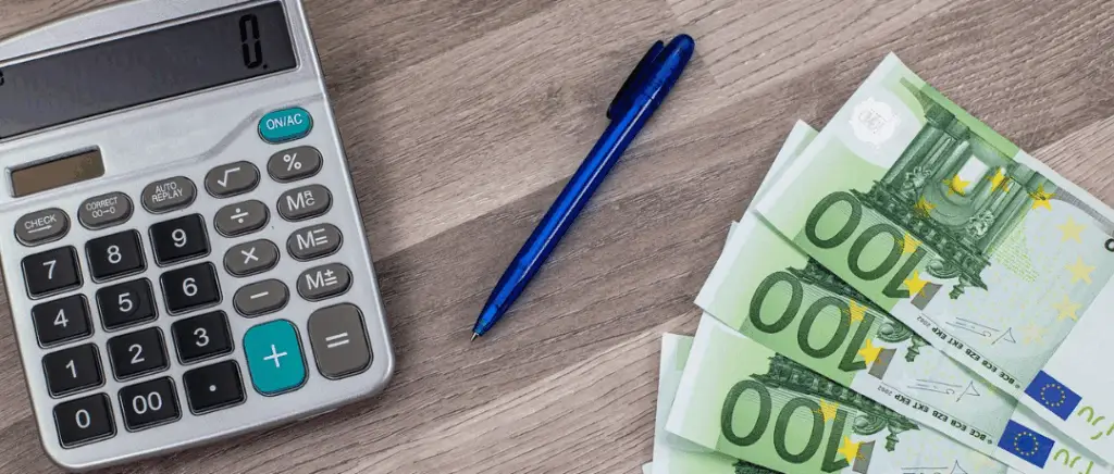 des billets de 100€ sont étalés sur une table à côté d'une calculatrice et un stylo