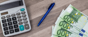 des billets de 100€ sont étalés sur une table à côté d'une calculatrice et un stylo