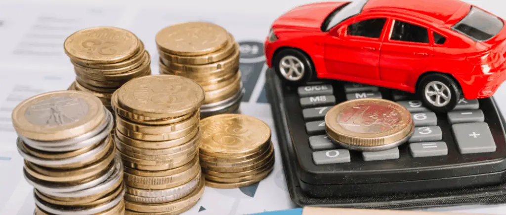 une voiture miniature est placée sur une calculette à côté d'une pile de pièces de monnaie